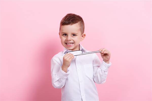 پسری شاد که در حال مسواک زدن است و تصویر کاغذی بزرگی از یک دندان و مسواک روی پس‌زمینه صورتی در دست دارد