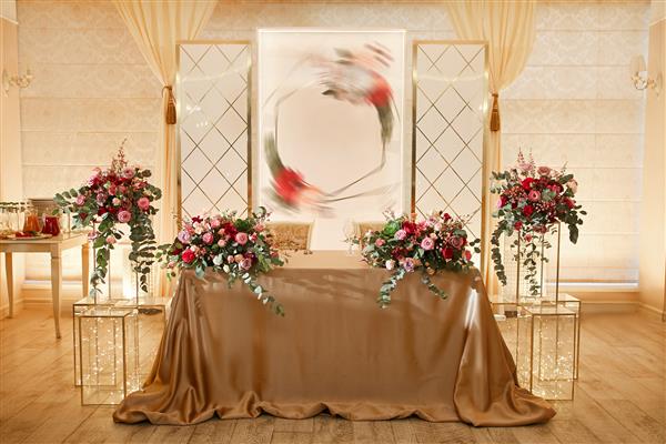 سفره عقد تازه عروس با رومیزی طلایی پوشیده شده است دسته گل های زیبا روی میز