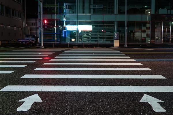 گذرگاه عابر پیاده با فلش های جهت دار در شب علامت گذاری عابر پیاده روی پیاده رو خیس سیگنال قرمز برای چراغ راهنمایی گذرگاه عابر پیاده روبروی ساختمان تجاری