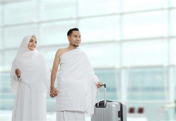 زن و شوهر مسلمان با لباس سنتی سفید برای احرام آماده پیاده روی حج در فرودگاه