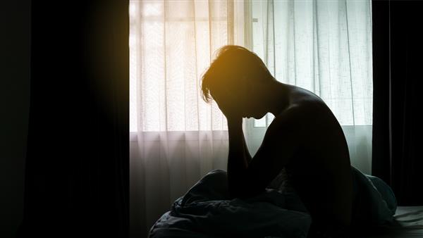 مرد افسرده سر در دست روی تخت در اتاق خواب تاریک نشسته است استرس افسردگی اختلال دوقطبی مفهوم