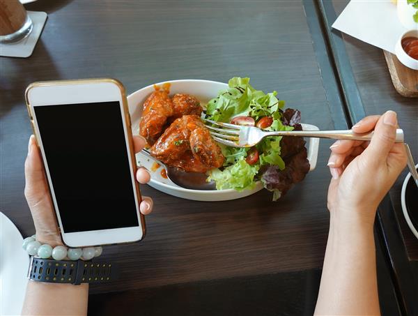 نزدیک دست زن با چنگال برای خوردن غذا و شیوه زندگی با استفاده یا نگاه کردن به گوشی هوشمندش و صرف ناهار در رستوران با دوستانش