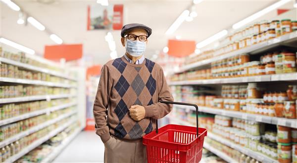 مرد ارشد با ماسک صورت پزشکی در سوپرمارکت خرید می کند