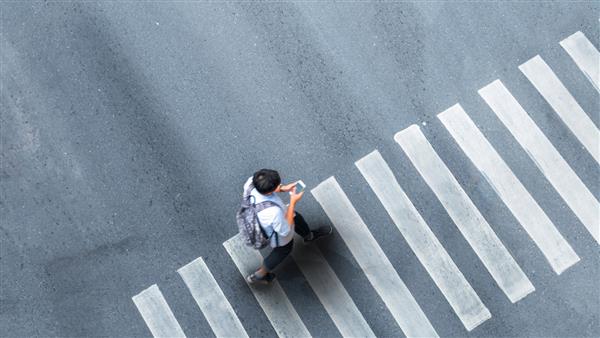 زندگی انسان در فاصله اجتماعی نمای بالای هوایی با مردی تار با گوشی هوشمند در حال راه رفتن در گذرگاه عابر پیاده در خیابان خاکستری پیاده رو با فضای خالی