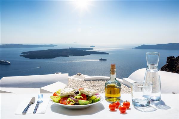 سالاد یونانی با روغن زیتون و گوجه فرنگی در مقابل منظره ای خیره کننده به دریای آبی و دریای اژه به عنوان مفهومی از غذاهای یونانی در تابستان