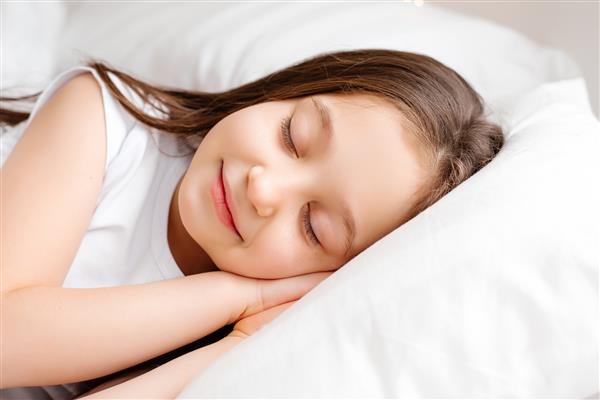 دختر سبزه کوچولو با ملافه سفید در رختخواب شیرین می خوابد فضایی برای متن خواب سالم کودک