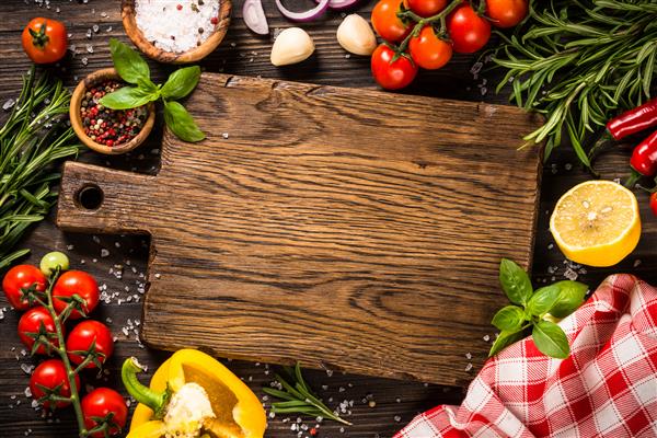 پس زمینه پخت غذا با تخته برش ادویه جات ترشی جات گیاهان و سبزیجات روی میز آشپزخانه چوبی نمای بالا با فضای کپی