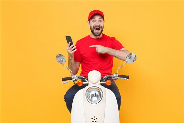 مرد تحویل‌دهنده با تی‌شرت کلاه‌ک قرمز یکنواخت رانندگی با موتور موتور سیکلت اسکوتر تلفن همراه جدا شده روی پس‌زمینه زرد استودیو کارمند مرد کارمند پیک خدمات قرنطینه مفهوم همه‌گیر کووید۱۹