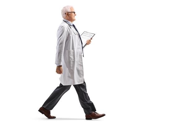 عکس نمایه تمام طول از یک پزشک بالغ که روی پس‌زمینه سفید راه می‌رود