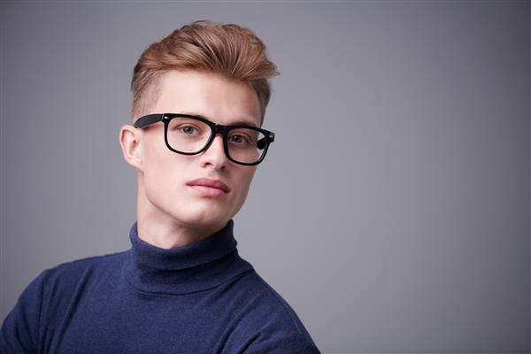 زیبایی مردانه پرتره یک مرد جوان خوش‌تیپ با موهای بور که عینک به چشم دارد روی پس‌زمینه خاکستری اپتیک برای مردان