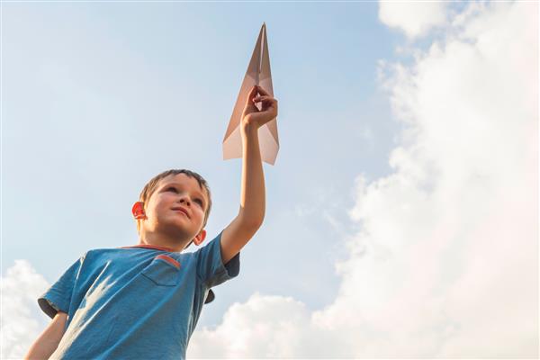 کودک شاد در حال بازی با هواپیمای کاغذی در برابر آسمان پسری با هواپیمای کاغذی