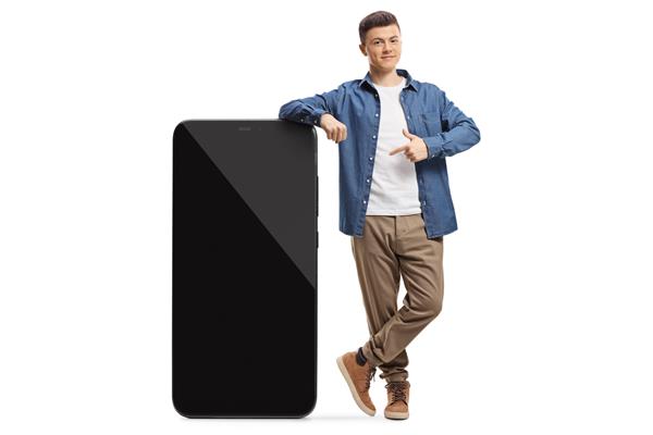 پرتره تمام قد از یک پسر معمولی که به یک تلفن هوشمند بزرگ تکیه داده و در پس زمینه سفید جدا شده است