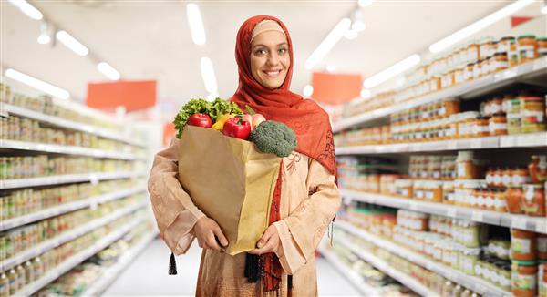زن جوان مسلمان با لباس های سنتی که یک سبد خرید در سوپرمارکت در دست دارد