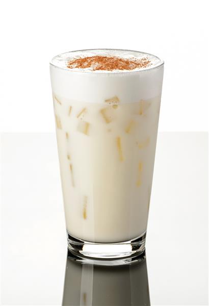 میلک شیک وانیل یخی با بستنی کف شیر و تکه های یخ پاشیده شده با دارچین در یک لیوان به سبک اروپایی در زمینه سفید