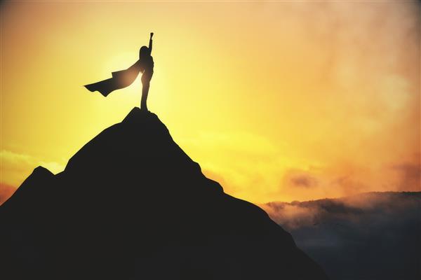 مفهوم موفقیت و رضایت با زن فوق العاده با کت تکان دادن بالای صخره تیره در پس زمینه آسمان مه آلود زرد