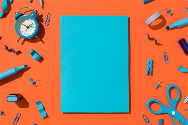 عکس نمای بالای کاغذ ورق آبی رنگی و لوازم التحریر آبی رنگ و لوازم مدرسه در پس زمینه نارنجی جدا شده با فضای خالی