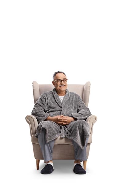مرد بالغ با لباس حمام و لباس خواب روی صندلی راحتی جدا شده در پس زمینه سفید نشسته است