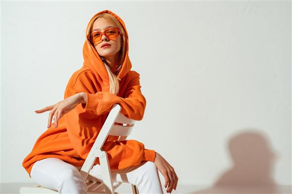 زن بلوند شیک و با اعتماد به نفس با پیراهن نارنجی مد روز عینک آفتابی رنگی ژست روی پس زمینه سفید کپی فضای خالی برای متن