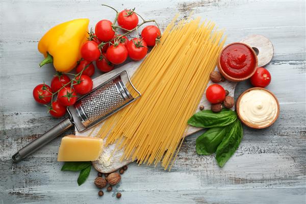 اسپاگتی پاستا با گوجه فرنگی پنیر و ریحان در زمینه چوبی رنگی