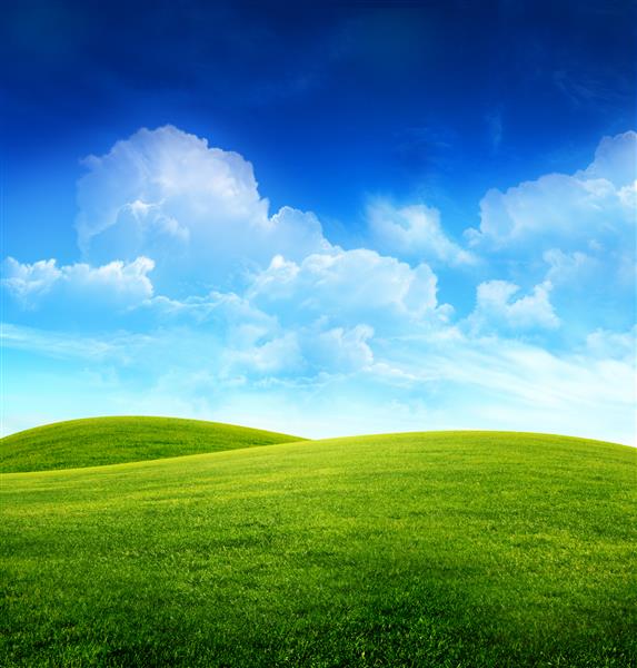زمین چمن سبز روی تپه های کوچک و آسمان آبی با ابرها