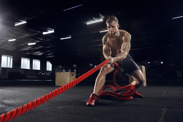 مرد جوان سالم ورزشکار در حال انجام ورزش با طناب در باشگاه