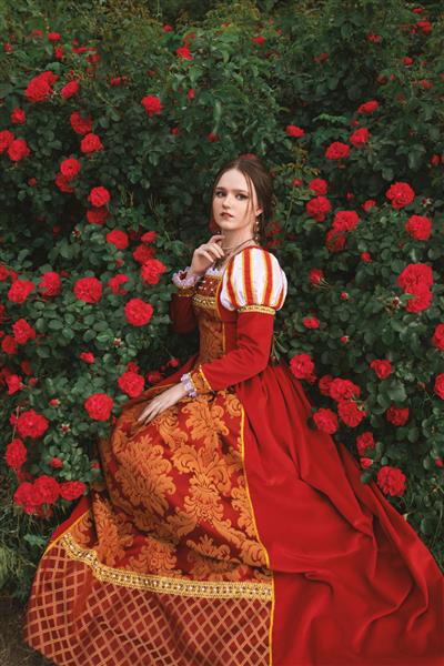 زن جوان با لباس قرون وسطایی قرمز در باغ با گل رز قرمز نشسته است