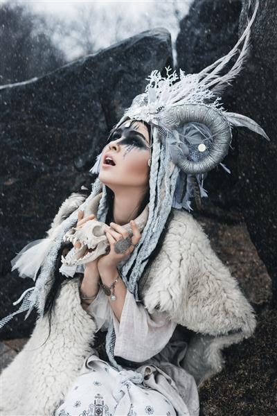 زن زیبا با آرایش فانتزی و تاج در برف نشسته است