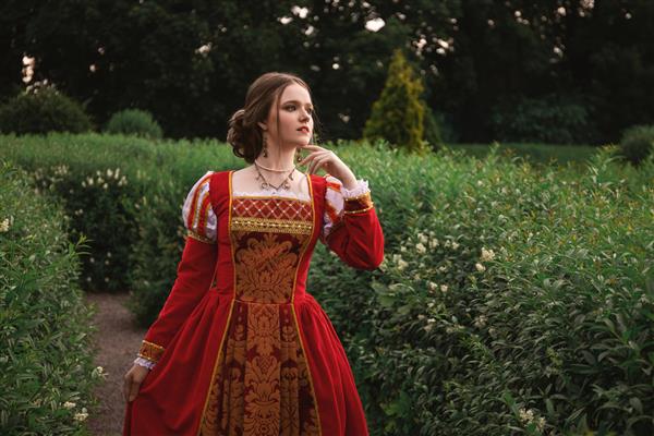زن جوان زیبا با لباس قرون وسطایی قرمز در باغ ایستاده است