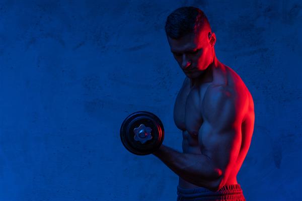 مرد بدنساز جوان و عضلانی در حال ورزش با دمبل در نور نئون رنگارنگ
