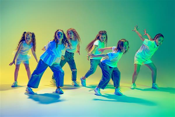 گروهی از بچه‌های فعال دختران شاد که روی پس‌زمینه سبز در نور نئون می‌رقصند
