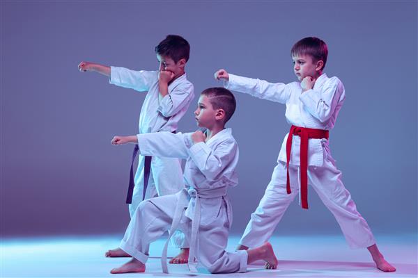 گروهی از کودکان پسر که کاراته هنرهای رزمی را تمرین می‌کنند روی پس‌زمینه استودیو بنفش در نئون جدا شده‌اند