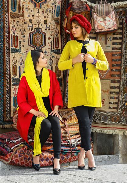 عکاس مدلینگ دو زن زیبای ایرانی با مانتو و شال زرد و قرمز در پس زمینه فرش ایرانی