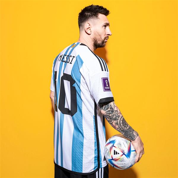 لیونل مسی با لباس تیم آرژلنتین و توپ فوتبال از نیم رخ در زمینه زرد