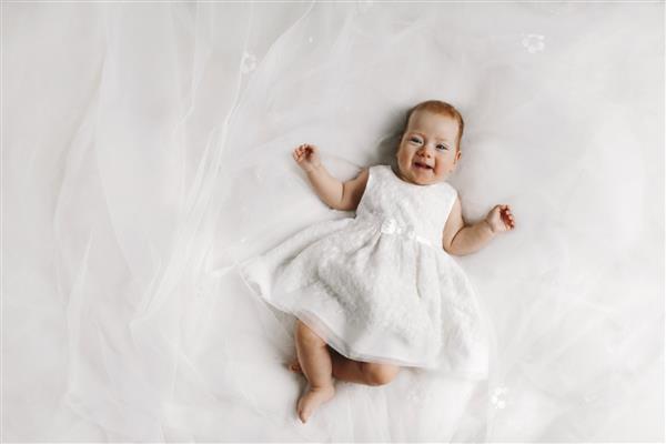 نوزاد دختر کوچکی که روی تخت دراز کشیده و لبخند می زند