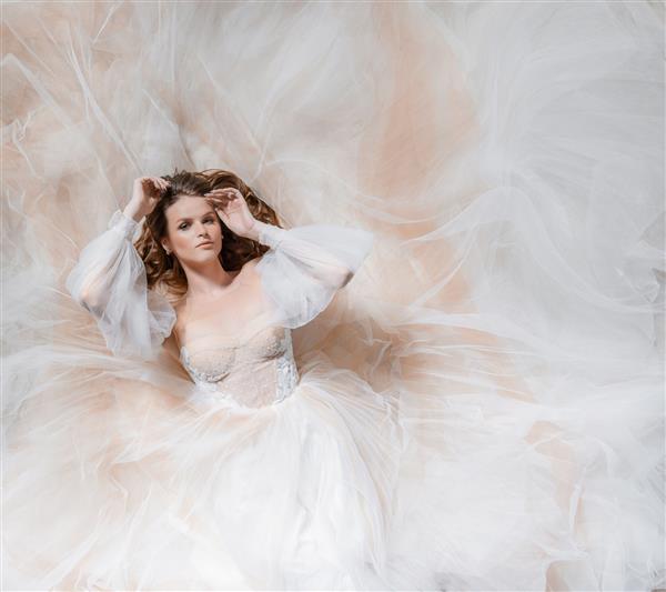 نمای هوایی عروس جوان زیبا که روی زمین دراز کشیده و به دوربین نگاه می کند دور تا دور لباس پارچه ابریشمی