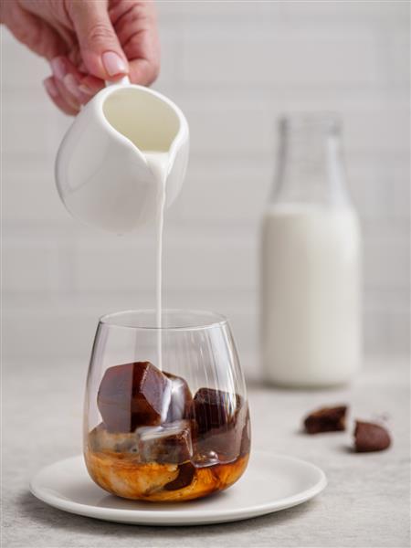 ریختن شیر در یک لیوان قهوه اسپرسو با مکعب های قهوه یخ زده در زمینه روشن