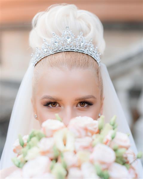 نمای نزدیک از یک عروس زیبا در یک تاج گرانبها با یک دسته گل در دستانش