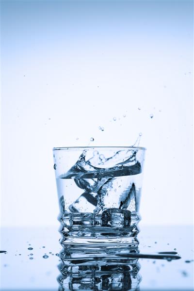 پاشیدن آب تمیز در یک لیوان با یخ در زمینه سفید