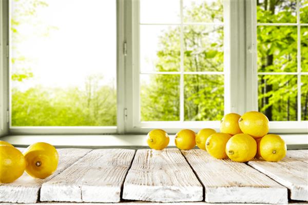 میز زمینه چوبی فضای آزاد با لیموی زرد تازه در بالا پس زمینه تار پنجره و چشم انداز باغ تابستانی عکس با فضای خالی برای لیوان یا بطری شما