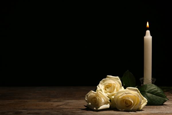 گل رز سفید زیبا و شمع روی میز در برابر پس زمینه سیاه نماد تشییع جنازه
