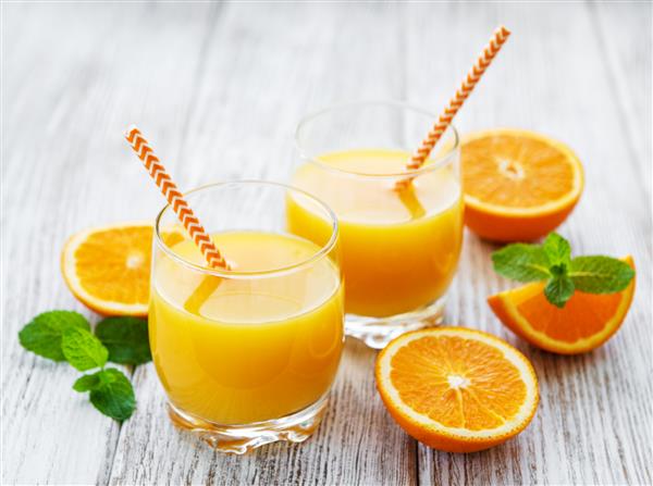لیوان های آب میوه و میوه های پرتقال روی میز چوبی