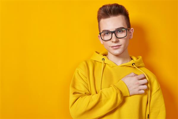مرد جوان باحالی با هودی زرد روشن و عینکی که روی پس‌زمینه زرد ژست گرفته است مد جوانان