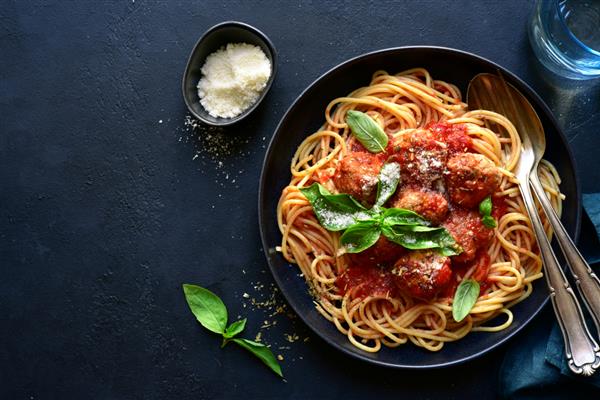 اسپاگتی با توپ های گوشتی در سس گوجه فرنگی در یک کاسه سیاه روی یک تخته سنگ تیره سنگ یا پس زمینه بتنی نمای بالا با فضای کپی