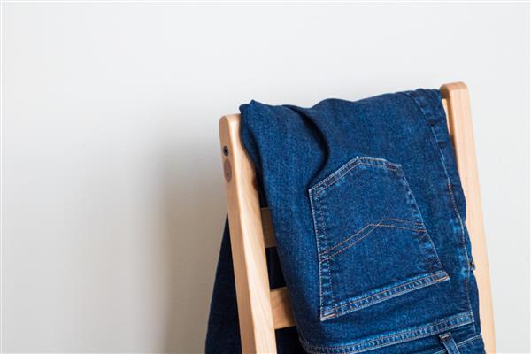 یک شلوار جین آبی تا شده روی یک صندلی چوبی پس زمینه سفید