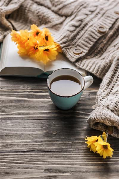 قهوه صبح بهاری یک فنجان قهوه روی میز چوبی و یک ژاکت گرم در پس زمینه ای از گل های زرد مفهوم طبیعت بی جان فضای کپی