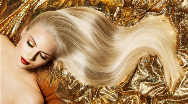 مدل مو بلوند زیبا موهای بلوند طلایی و صاف براق از نزدیک آرایش صورت زنانه لوکس Glamour Perfect Skin زن مد روی پارچه طلایی دراز کشیده است