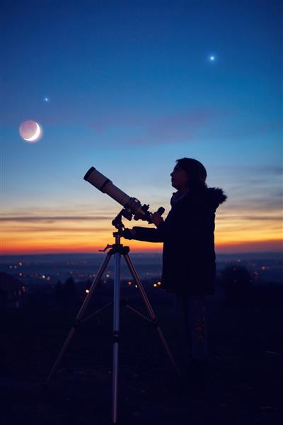 دختر بچه در حال رصد ستارگان سیارات ماه و آسمان شب با تلسکوپ نجومی