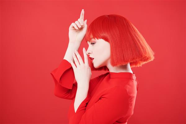 دختری شایان ستایش با لب های قرمز روشن و موهای قرمز که در پروفایل ژست گرفته است پس زمینه قرمز استودیو زیبایی آرایش مدل مو رنگ مو رنگ قرمز مد روز
