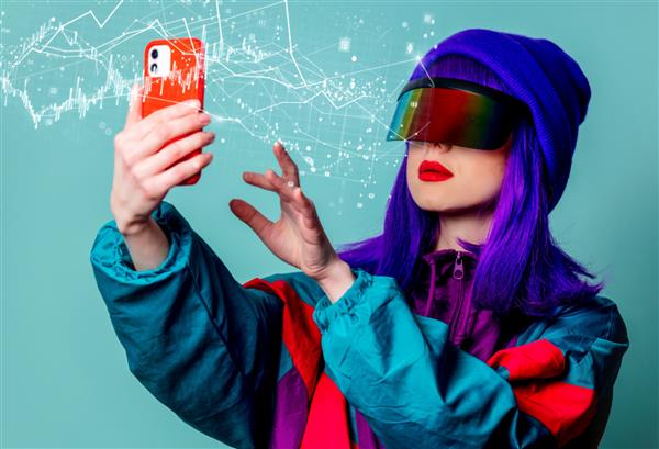 دختر شیک با عینک پانک سایبری و لباس ورزشی دهه 80 با استفاده از تلفن همراه در پس زمینه آبی
