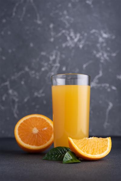 آب پرتقال تازه در شیشه با میوه های نارنجی رسیده در پس زمینه تیره
